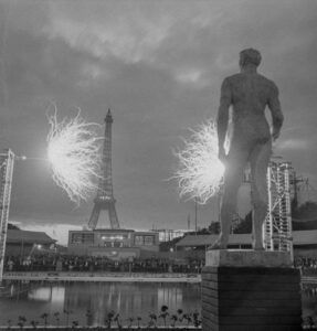 Etincelle réalisée en haute fréquence. Longueur 7 m, puissance 200Kw, plusieurs millions de Volts, réalisation par la CPDE. Au premier plan, la statue de Zeus. Au fond, dans l’axe de la tour Eiffel, la cabine de projection.